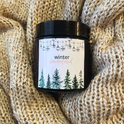 Svíčka Kiskedves Winter Wonderland na pletené dece, dobře je vidět akvarelový štítek s lesem.